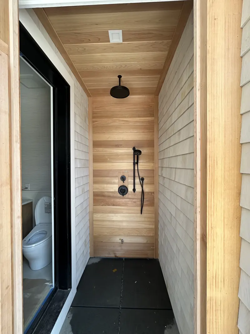 Outdoor shower lined with cedar boards, with a matte black ceiling rain head, handheld shower and valve trim