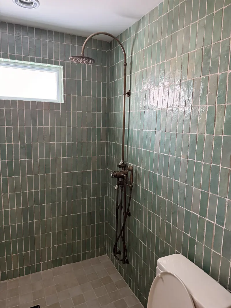 Antique-brass exposed shower with a curved riser, rain head and handheld on green zellige-style tile
