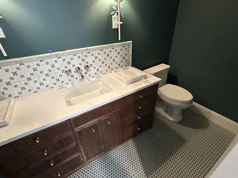 Powder room with deep green walls, a wall-mounted polished faucet over an undermount sink, a patterned tile backsplash and a toilet