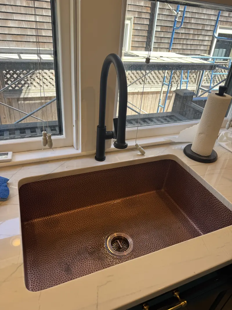 Hammered copper undermount kitchen sink with a matte black pull-down faucet under a window